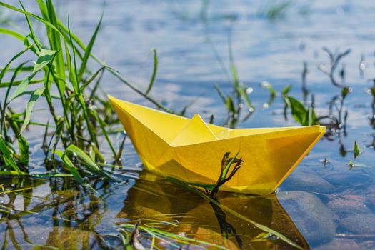 Yellow paper boat aground near the river bank in the grass. Origami as a hobby