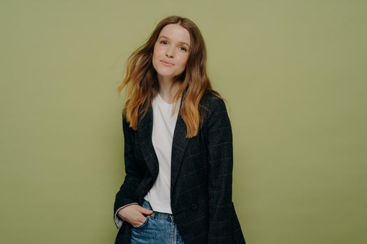 Stylish nice looking young female student wearing fashionable clothes posing with hand in pocket on color background, charming teenage girl in casual clothes expressing positive emotions