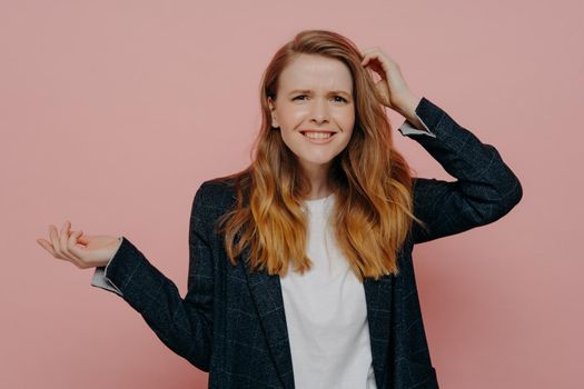 It can not be true. Portrait of young frustrated woman touching head with confused expression, can not believe what she hearing or seeing, dressed in plaid jacket and standing on pink background