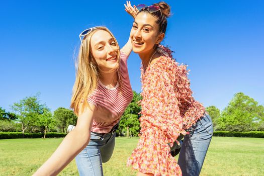 Two women best friends having fun in a city park posing for a happy selfie smiling looking at camera. Two homosexual student girl enjoying diversity joking together outdoor in the green of nature