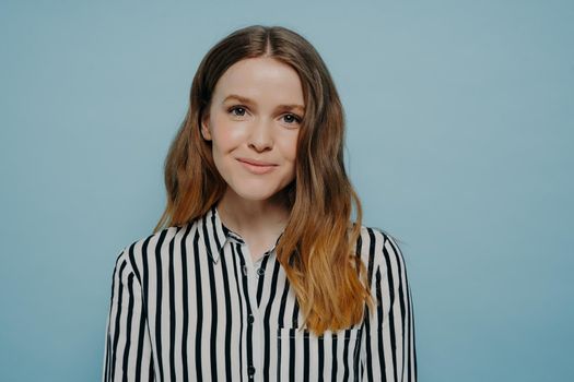 Headshot of cute happy smiling millennial girl wearing striped shirt looking at camera with pleasure while posing on turquoise background, positive pretty female expressing good emotions