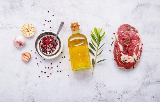 Raw Rib Eye steak set up  on white concrete background. Flat Lay of fresh raw beef steak with rosemary and spice on white shabby concrete background top view.