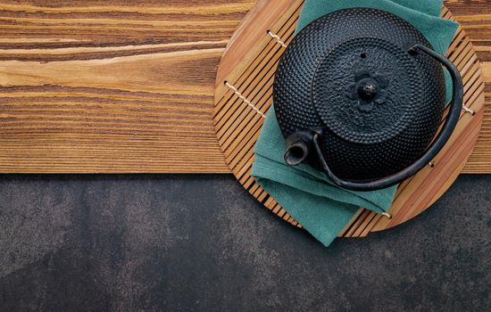 Black cast iron tea pot with herbal tea set up on dark stone background.