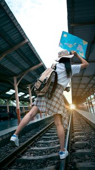 Young Female tourists are happy to travel. Traveler woman with a backpack, camera, map walking on railroad tracks. Pretty girl feels exciting.