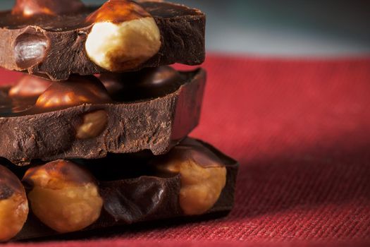 Slices of natural black chocolate with hazelnuts on a red napkin. Close-up macro view