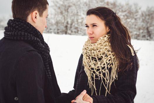 A guy and a girl in warm clothes and scarves on a walk in the snowy forest and in the field