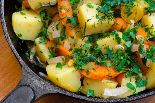 Fried potatoes with vegetables sprinkled with chopped parsley in a cast-iron frying pan on a wooden board