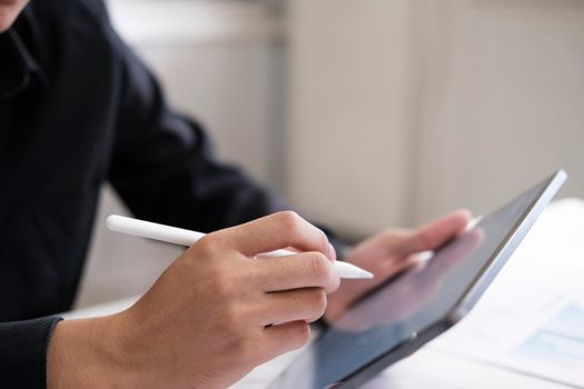 Closeup man with stylus pen writing on digital notepad, touching on digital tablet screen working on laptop computer in office. Web designer working his project. Paperless business, technology