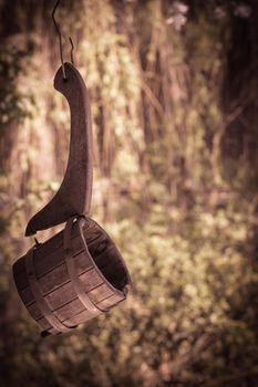 Old broken wooden ladle for russian bath hanging on a wire against a foliage background. Vintage look