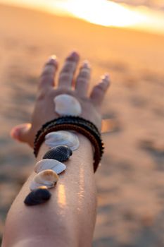 Woman holds seashells on her hand and points towards the sea. Sunrise on the beach in the early morning