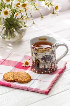 Still life with a cup of tea, cookies and daisies on a wooden background in morning sunlight