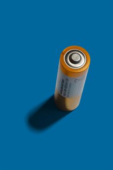 Alkaline AA orange metallic battery top view on blue background