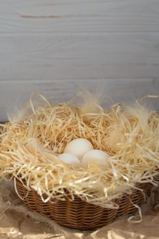 Chicken eggs lie on a wicked paper straw in a wicker basket on a dark wooden background in the morning sun
