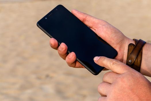 A man touching smartphone screen with his index finger on a beach sand background