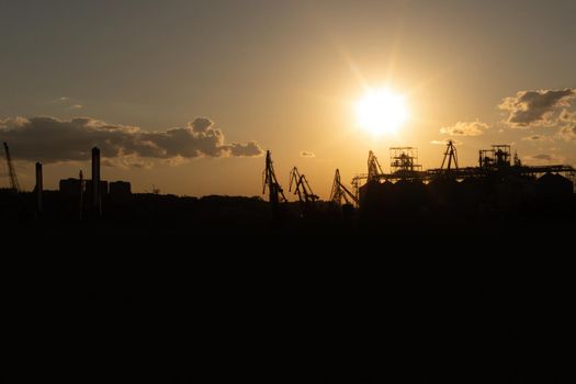 Silhouette of a cargo port at sunset on the Black Sea coast, Odessa, Ukraine. View from afar on loading cranes and containers