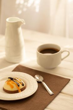 Still life with a cup of coffee and sweet cake on white wooden table. Breakfast in the morning sun