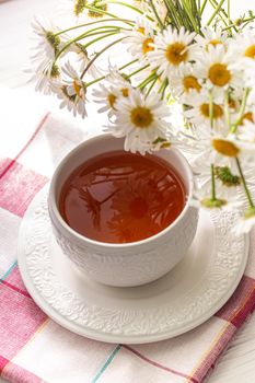 Still life with a cup of tea, cookies and daisies on a wooden background in morning sunlight