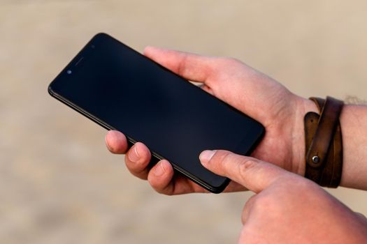 A man touching smartphone screen with his index finger on a beach sand background