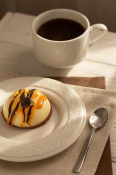 Still life with a cup of coffee and sweet cake on white wooden table. Breakfast in the morning sun