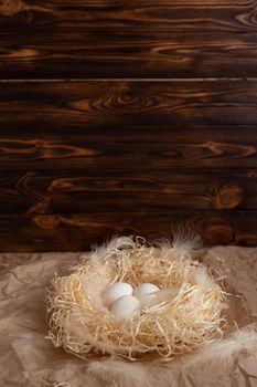 Chicken eggs lie on a wicked paper straw in a wicker basket on a dark wooden background in the morning sun