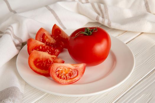 Ripe red tomatoes on a ceramic plate in a linen towel under soft sunlight
