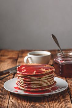 Stack of pancakes with berry jam on white plate over wooden table