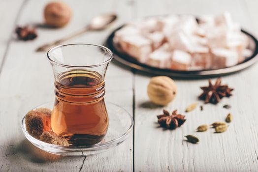 Tea in arab glass with turkish delight Rahat Lokum and different spices over wooden surface