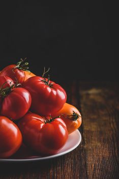 Fresh red and yellow tomatoes on white plate over wooden surface