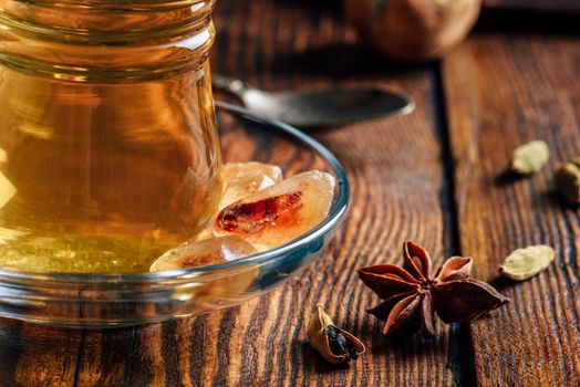 Spiced tea with star anise, cardamom and dried lime in oriental glass over wooden surface