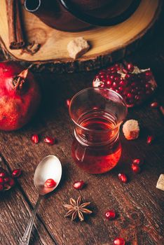 Black tea in arabic tea glass with fresh pomegranate and some spices on wooden table