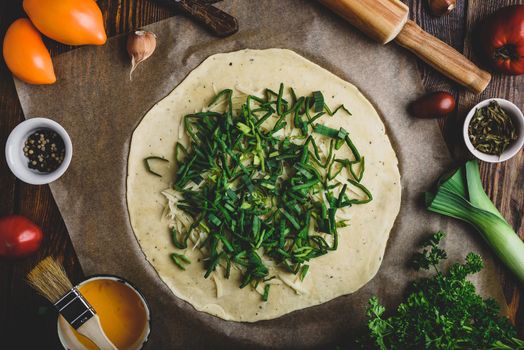 Rolled dough with grated parmesan cheese and sleced leek for preparing galette