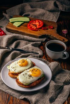 Bruschettas with vegetables and fried eggs on white plate and cup of coffee over grey rough cloth. Healthy food concept.