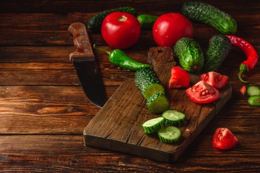 Sliced vegetables. Tomatoes, cucumbers and chili peppers over wooden background.