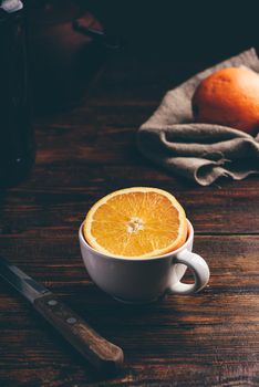 Half of orange in a white cup over rustic table