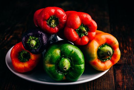 Multicolored fresh bell peppers on plate over wooden background