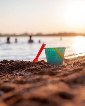 Children's toys for playing on the sand. Plastic bucket and rake on the beach at sunset. The concept of summer, family holidays and vacations.