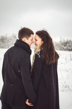 A guy and a girl in warm clothes and scarves on a walk in the snowy forest and in the field