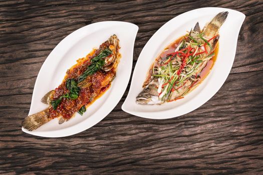 Fried fish with spicy salad in plate on wooden table with copy space.