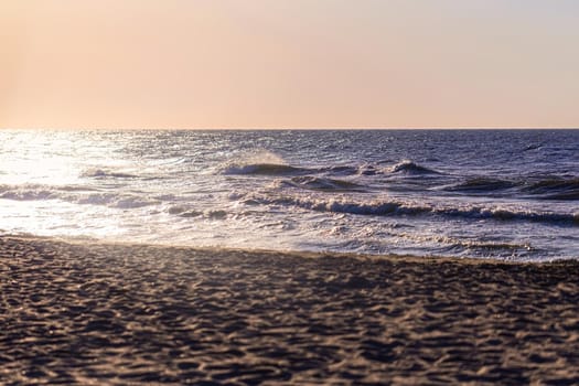 Sea horizont and sand beach at early morning sunrise. Small waves in sunlight