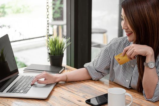 Asian girl making online payment using laptop for shopping at home, famle holding credit card.