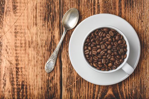 Roasted coffee beans in cup over wooden surface