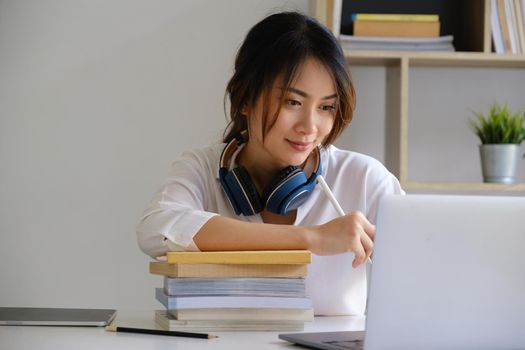Cheerful young asian woman using laptop computer at home. Student female in living room. online learning, studying , online shopping, freelance, asean concept.