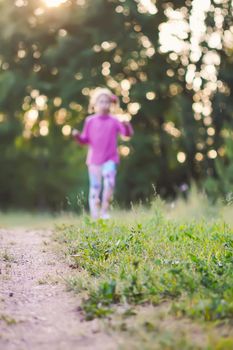 Running little girl silhouette behind the grass on summer field in countryside