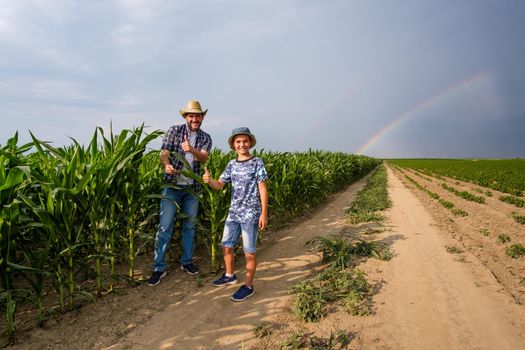 Father is teaching his son about cultivating corn. Corn plantation successfully sown. Farmers in agricultural field.