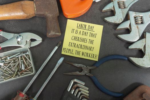 Text on yellow notepad with repair equipment and many handy tools on a dark background. Labor day concept