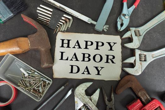 Happy labor day text on yellow notepad with repair equipment and many handy tools on a dark background