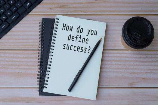 Text written on notepad with pen and coffee on wooden table. How do you define success