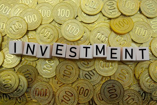 Investment text on wood block with a pile of gold coins