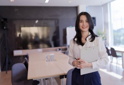 Portrait of Asian young beautiful business woman in the office. Crossed arms and holding Files, documents and pencil.