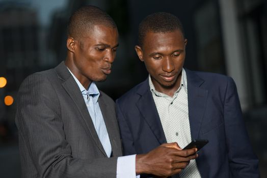 two african businessmen sending message on a phone in the street at night